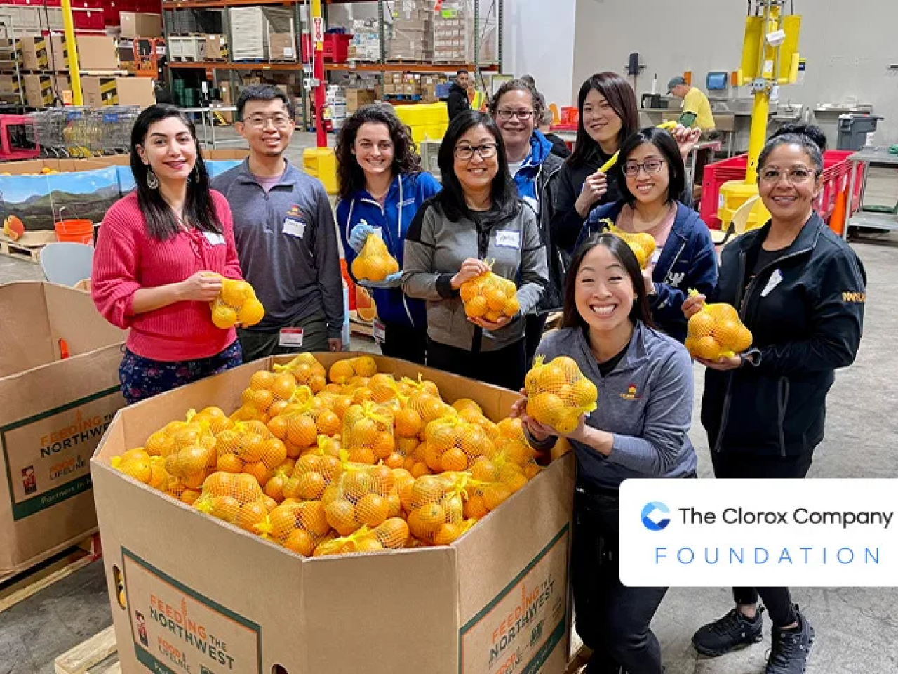 Smiling group of people standing around a pallet of oranges