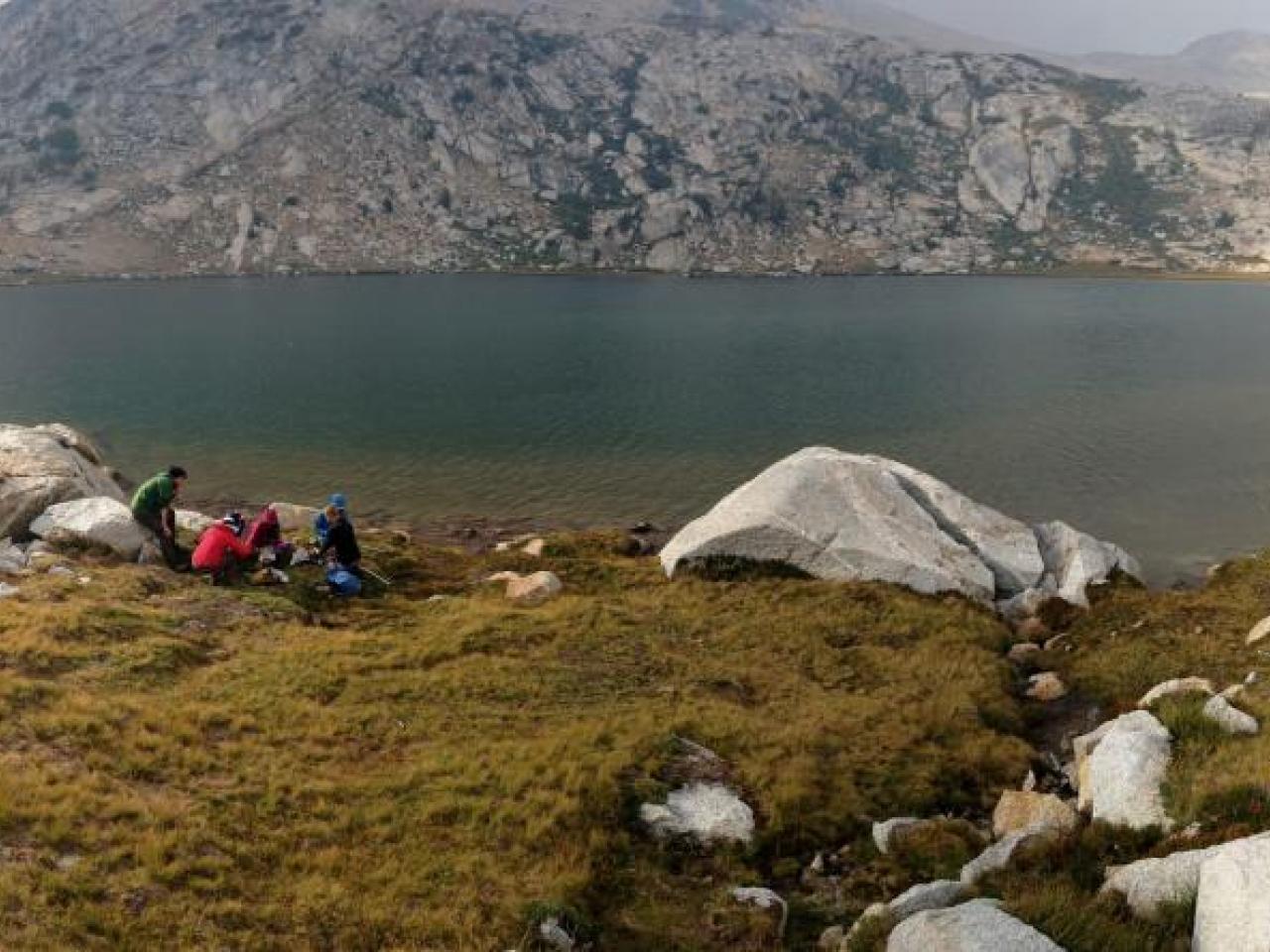 People at the edge of a body of water in mountainous terrain.