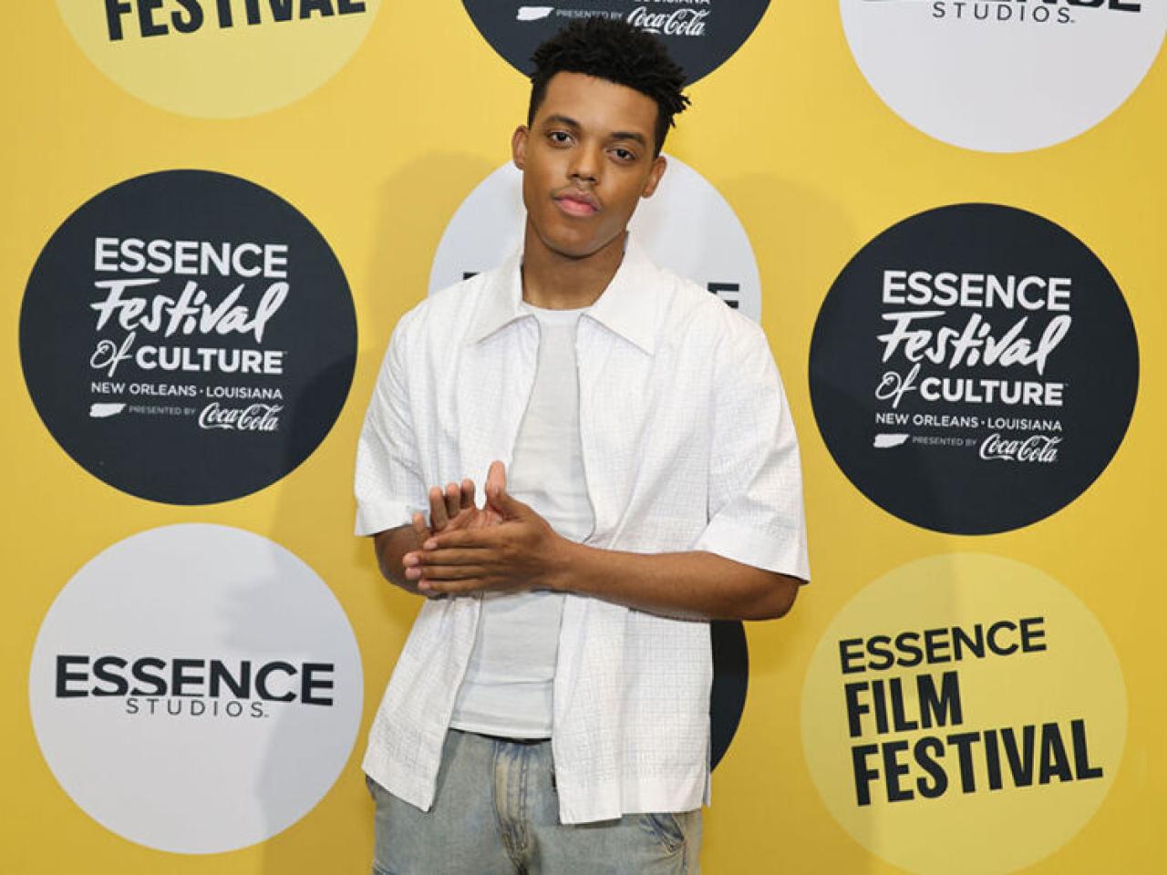 A person standing, facing the camera in front of a yellow backdrop with Essence Film Festival logos.
